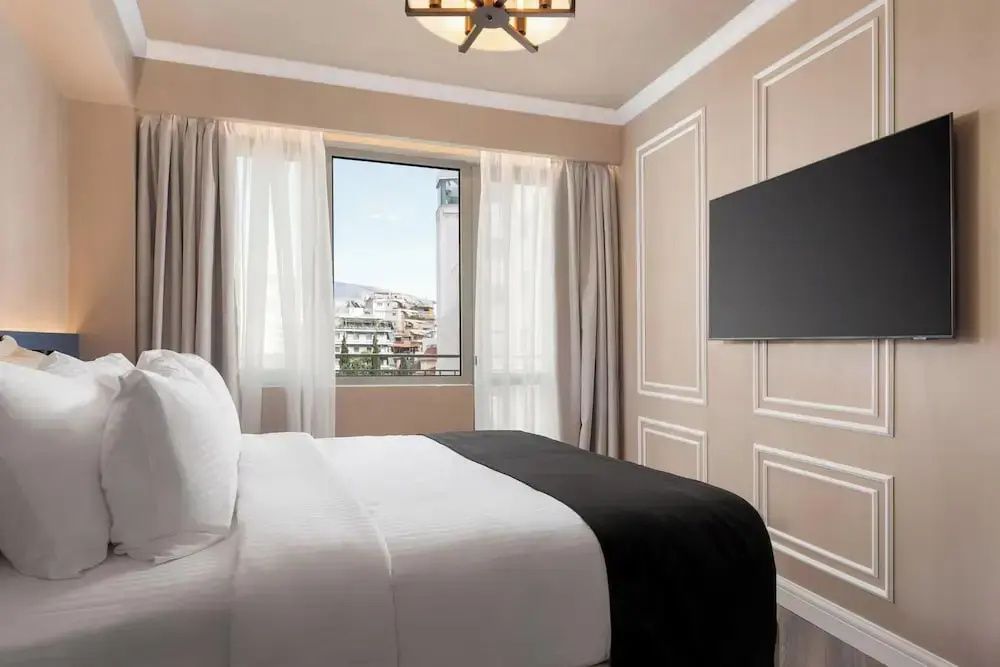 Doppelbett und Flachbildfernseher vor einem Fenster mit Blick auf die Stadt.