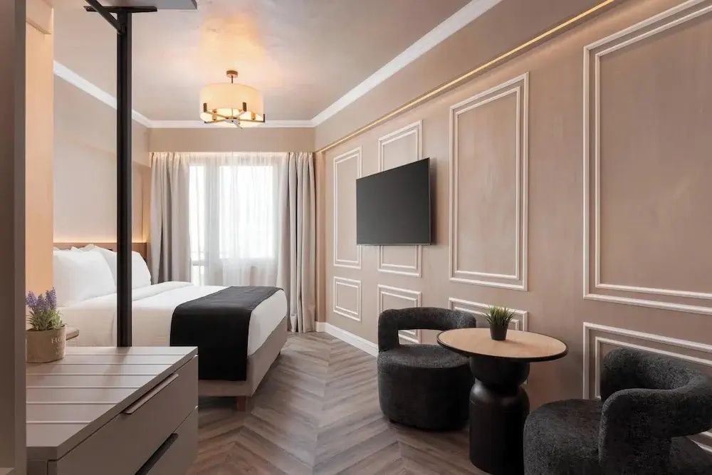 Modernes Hotelzimmer mit Doppelbett, Flachbild TV an verzierter Wand und Sitzbereich.