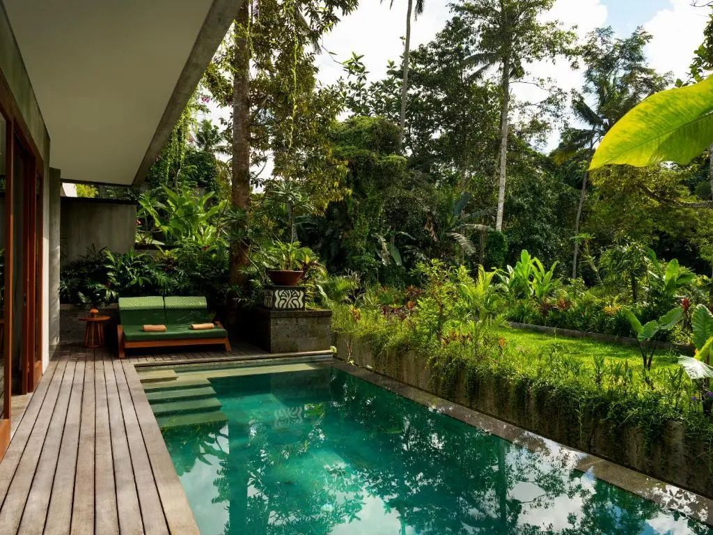Privater Pool mit Holzterrasse, Sonnenliegen und tropischer Gartenumgebung.