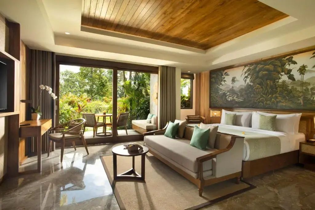 Geräumiges Hotelzimmer mit Doppelbett, Sofa, Holzdecke und großem Fenster zum tropischen Garten.