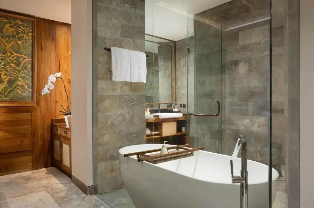 Modernes Badezimmer mit freistehender Badewanne, Glasdusche und Wänden aus Naturstein.
