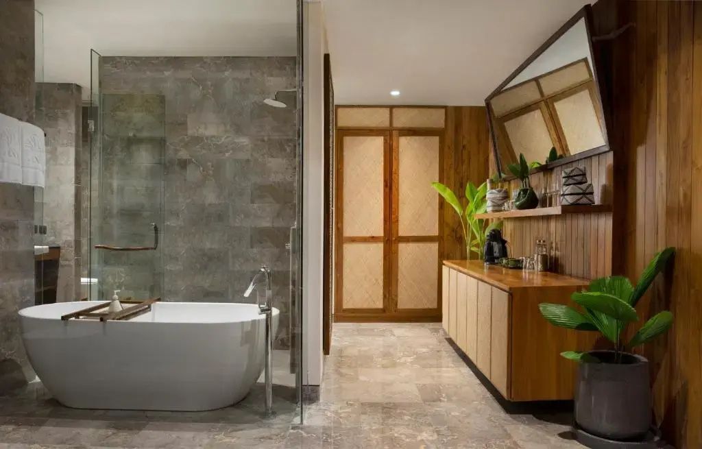 Badezimmer mit Holzschrank, spiegelnder Wand, hellen Fliesen und transparenter Duschwand.