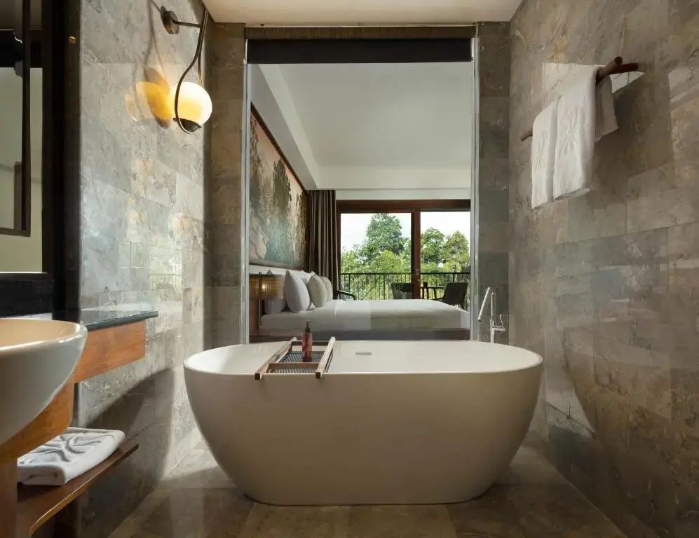 Freistehende Badewanne aus Stein in einem Badezimmer mit Blick ins Schlafzimmer.