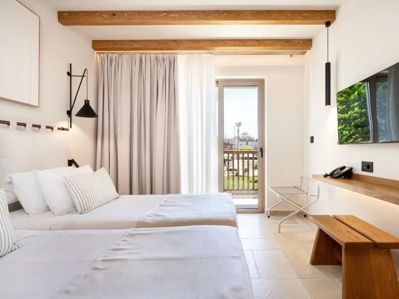 Helles Schlafzimmer mit zwei Betten, Holzbalken und Balkonausgang.