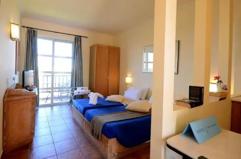 Schlafzimmer mit zwei blauen Betten, einem Kleiderschrank und Zugang zum Balkon.