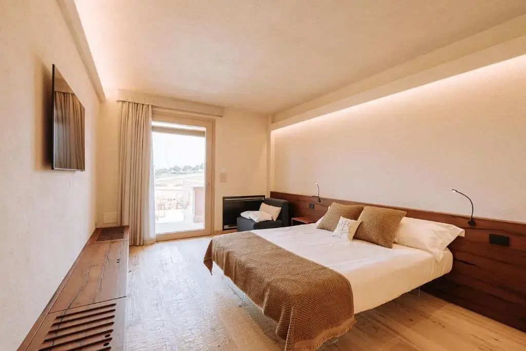 Helles Hotelzimmer mit Doppelbett, Holzfußboden und Zugang zur Terrasse.
