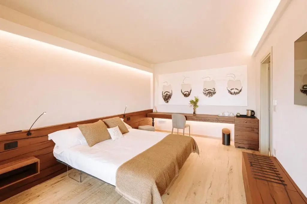 Helles Hotelzimmer mit Doppelbett, Schreibtisch und moderner Beleuchtung an den Wänden.