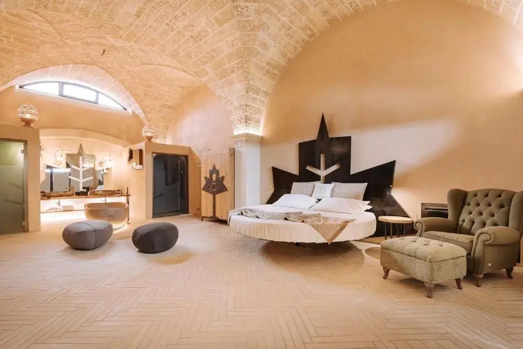 Weiträumiges Zimmer mit historischem Gewölbe rundem Bett Holzschrank und Wellnessbereich.