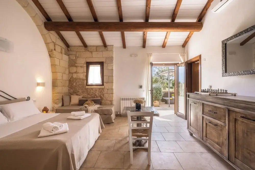 Rustikales Schlafzimmer mit Holzbalkendecke, Natursteinwand und geöffneter Tür zur Terrasse.