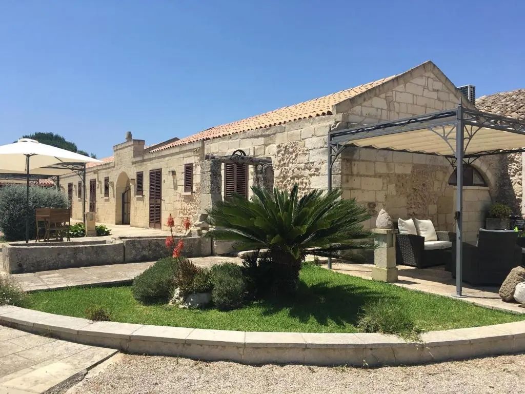Historisches Steingebäude der Masseria mit gepflegtem Garten und überdachter Terrasse.