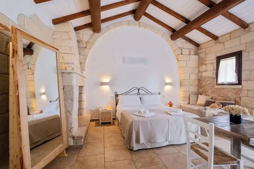 Helles Hotelzimmer mit großem Steinbogen, Doppelbett, Standspiegel und freigelegten Holzbalken.