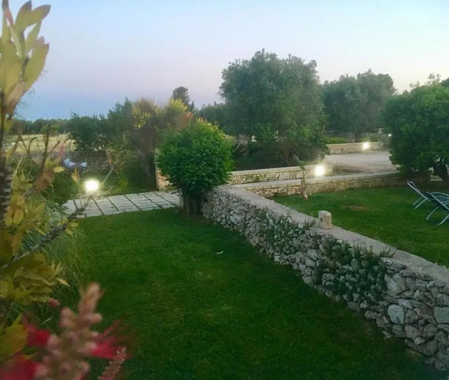 Gartenanlage mit einer gepflasterten Mauer, Rasenfläche und mediterranen Pflanzen.