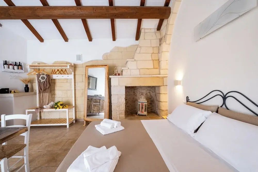Schlafzimmer mit Kamin aus Naturstein, Standspiegel und Garderobenständer neben dem Bett.
