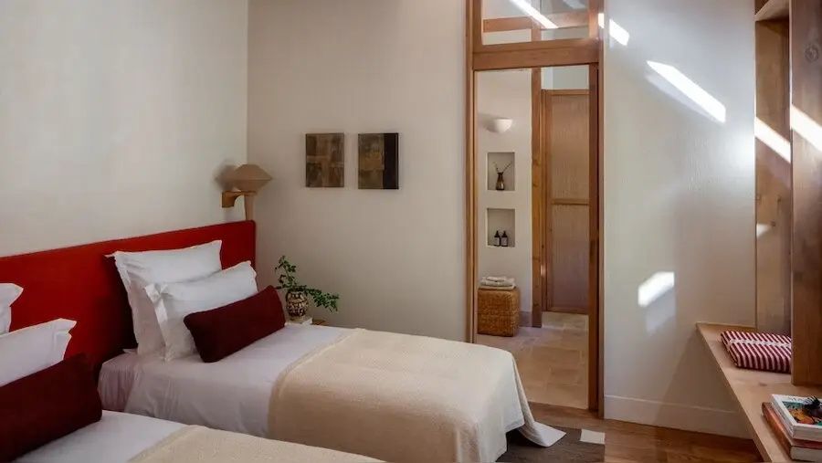 Hell eingerichtetes Schlafzimmer mit Bett, rotem Kopfteil und Blick ins Badezimmer.