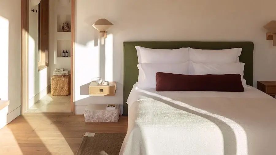 Doppelbett mit grünem Kopfteil, weiße Kissen und Sonnenlicht im Schlafzimmer.