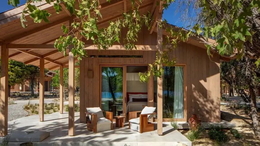 Holzhaus mit überdachter Terrasse, zwei Sesseln und großen Glasschiebetüren.