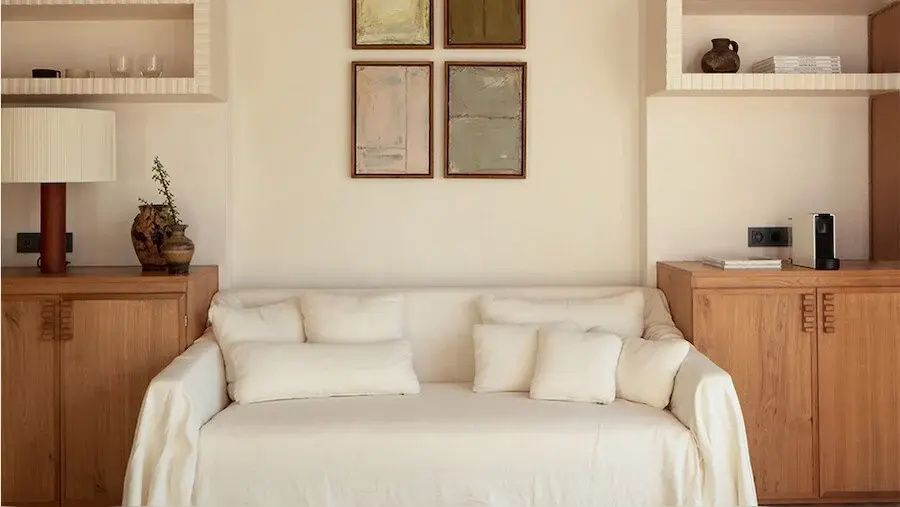 Heller Wohnbereich mit weißem Sofa, vielen Kissen und Wandbildern.