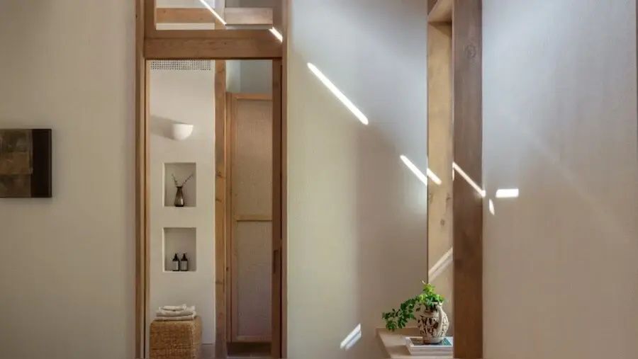 Nahaufnahme einer hellen Wand mit Nischen, Holzrahmen und Lichteinfall.
