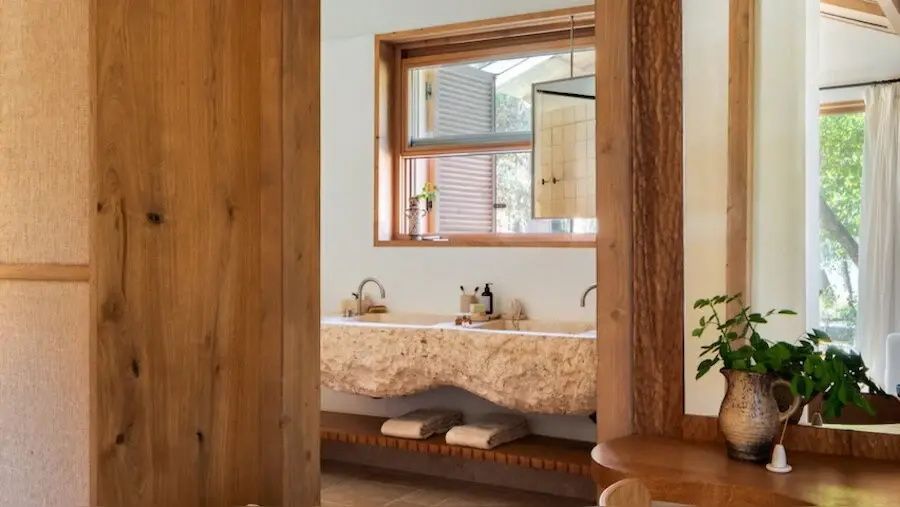 Badezimmer mit doppeltem Waschtisch aus Naturstein, Holzregal und Handtüchern.