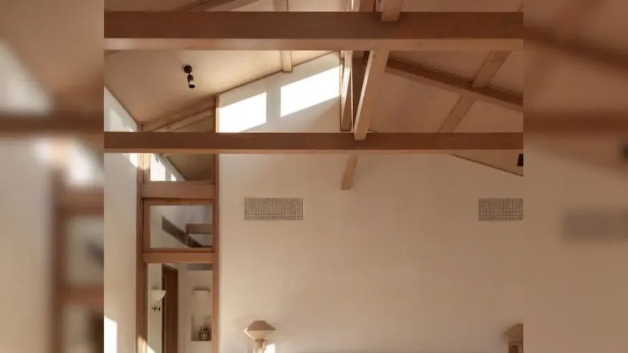 Hohe helle Zimmerdecke mit sichtbaren Balken aus Holz und obenliegenden Fensterfronten.