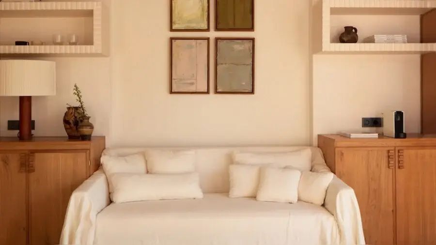 Helles Stoffsofa mit mehreren Kissen unter vier Kunstdrucken an der Wand.