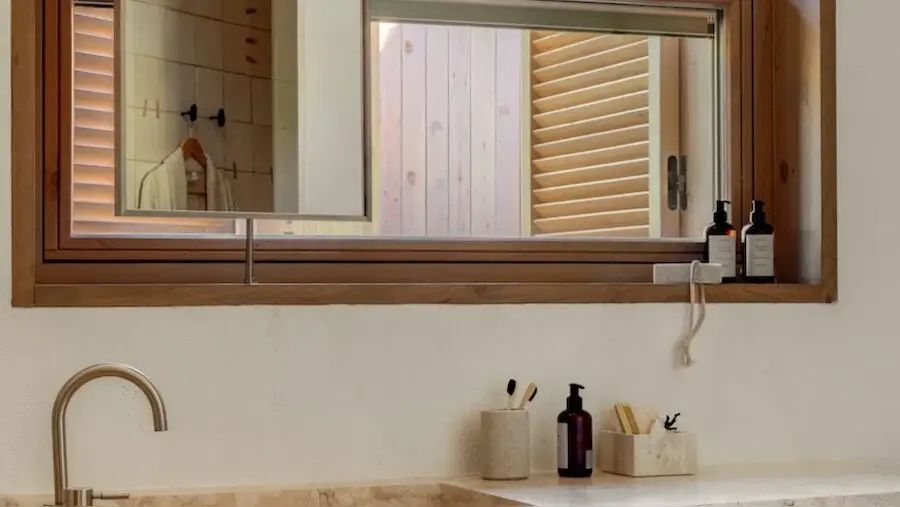 Waschtisch mit Zahnputzbechern, Seifenspender und Holzfensterrahmen im Badezimmer.