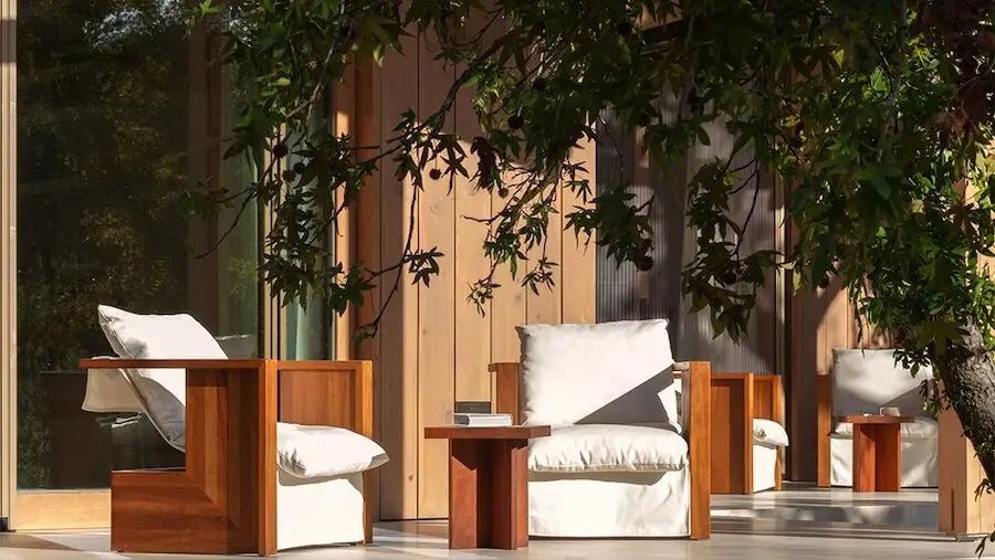 Holzsessel mit weißen Polstern auf einer schattigen Terrasse aus Holz.