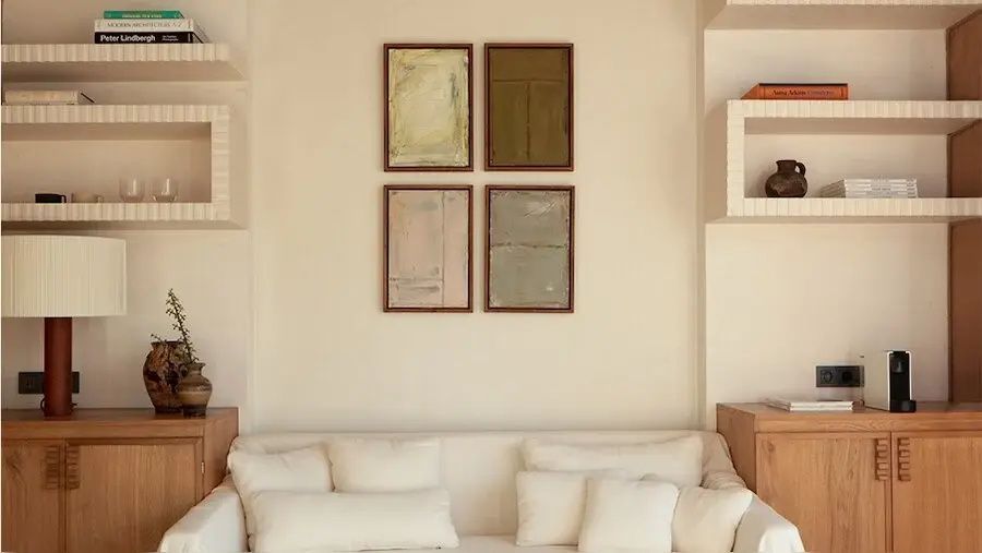 Vier gerahmte Bilder an einer hellen Wand über einem Sofa mit weichen Kissen.
