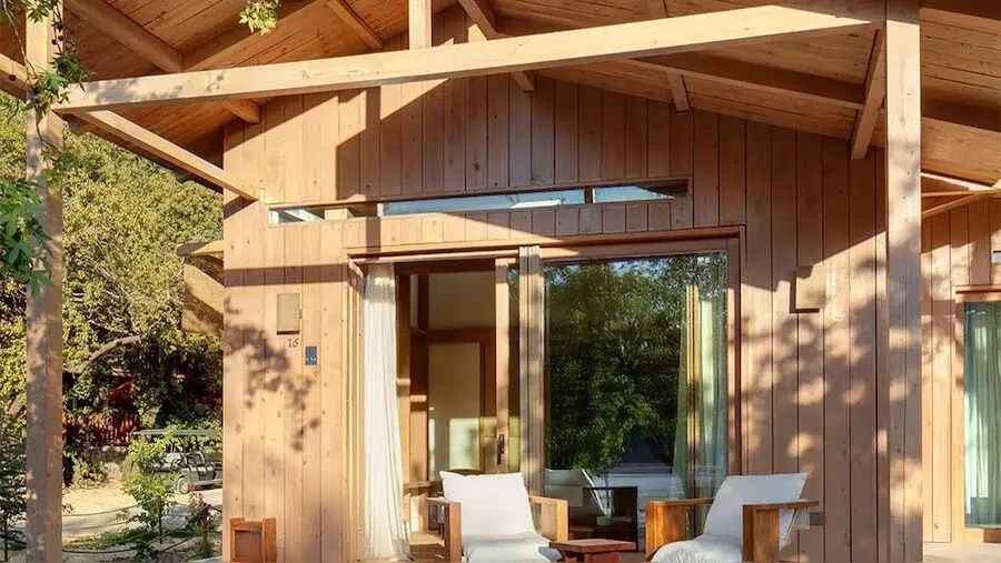Holzhaus mit Terrasse, großen Glastüren und Sitzgelegenheiten im Freien.