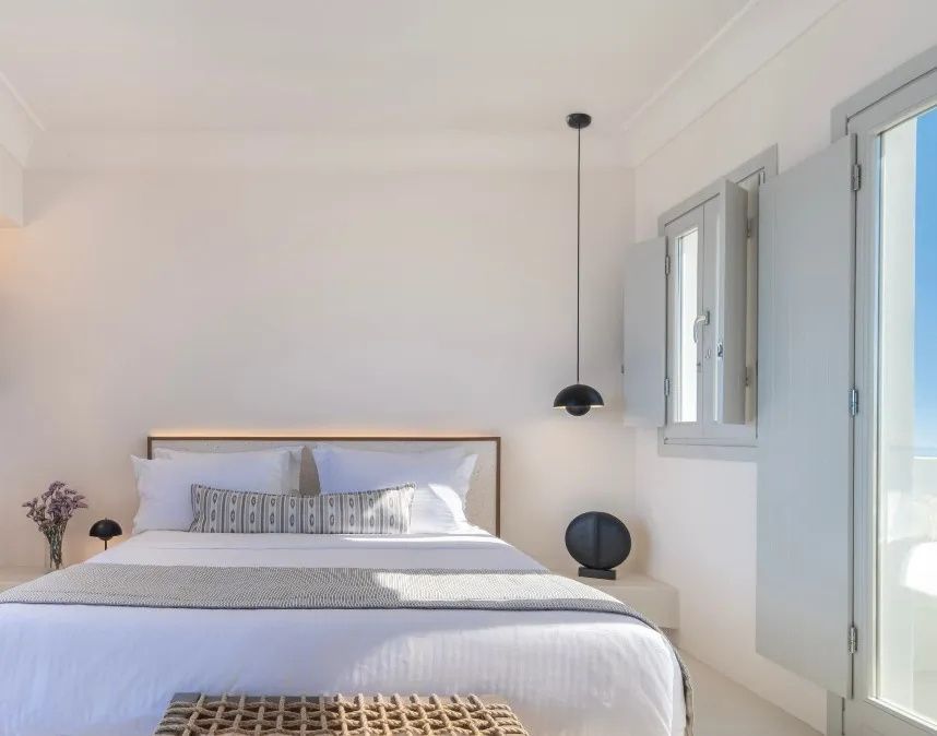 Heller Schlafraum mit Doppelbett, schwarzer Pendelleuchte und grauem Fensterladen.