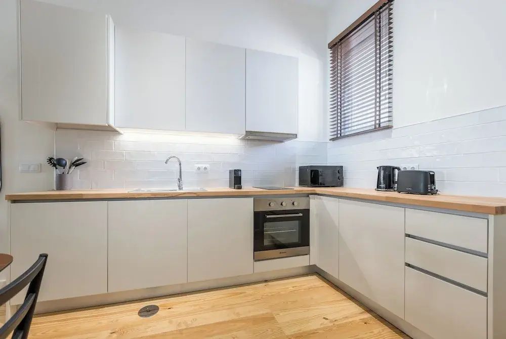 Moderne weiße Einbauküche mit Holzarbeitsplatte, Backofen und Wasserkocher.