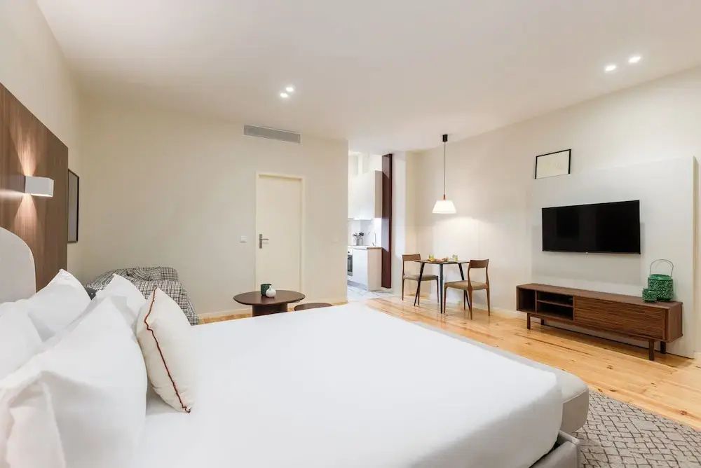Offenes Studio mit Doppelbett im Vordergrund, TV-Möbel und kleinem Esstisch im Hintergrund.