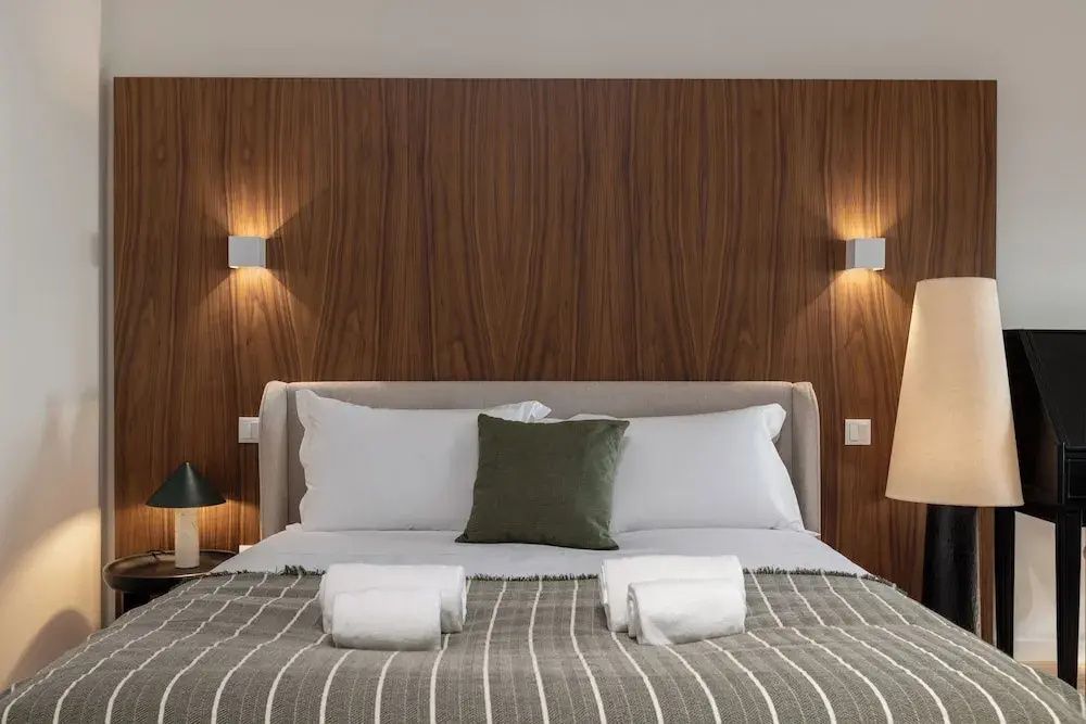 Doppelbett mit Kissen und Handtüchern vor einer dekorativen Holzverkleidung.