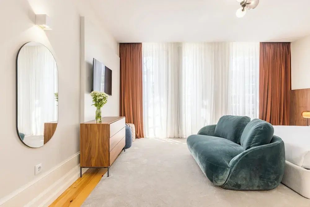 Wohnbereich mit grünem Samtsofa, Holzkommode und Flachbildfernseher an der Wand.