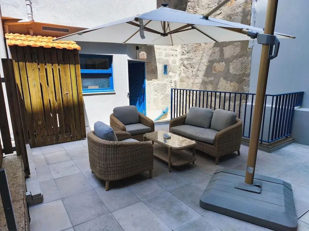 Gepflasterte Terrasse mit Rattansitzmöbeln und Sonnenschirm im Innenhof.