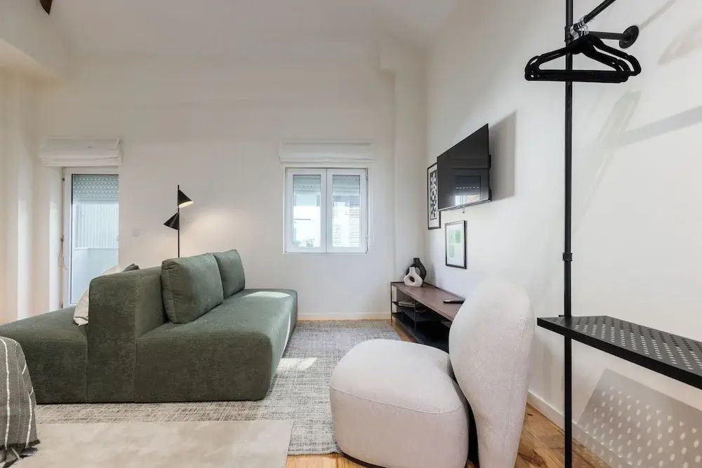 Helles Wohnzimmer mit grünem Sofa, weißem Sessel und Wandfernseher.