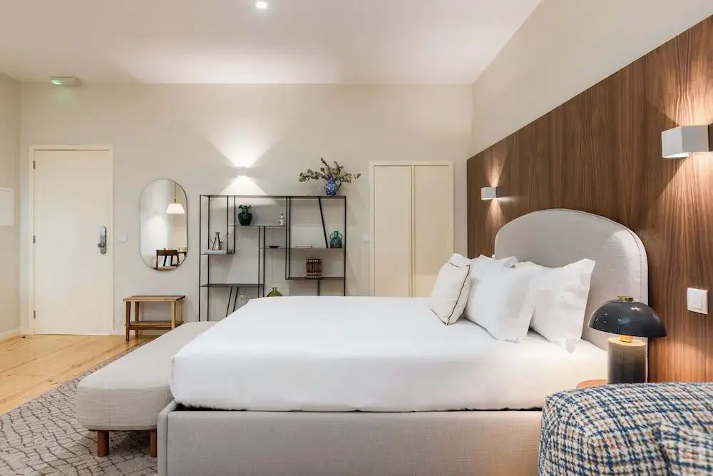 Seitenansicht eines Doppelbetts mit hellem Bettzeug und offenem Blick ins Zimmer.