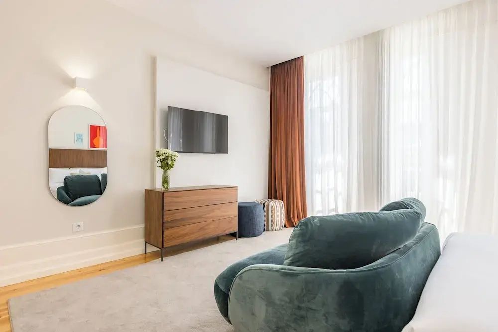 Blick von einem grünen Sofa auf eine Holzkommode mit Fernseher an der Wand.
