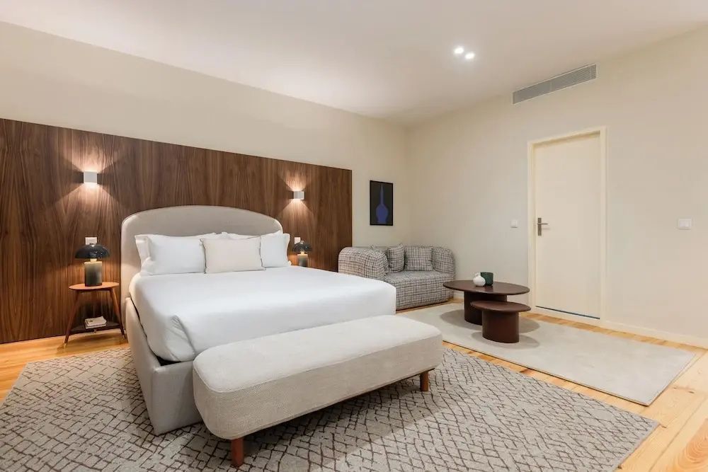 Doppelbett mit Sitzbank davor, Ecksofa und Couchtischen auf hellem Teppich.