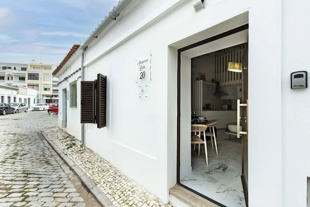 Weiße Außenfassade der Unterkunft mit geöffneter Eingangstür und hölzernen Fensterläden.