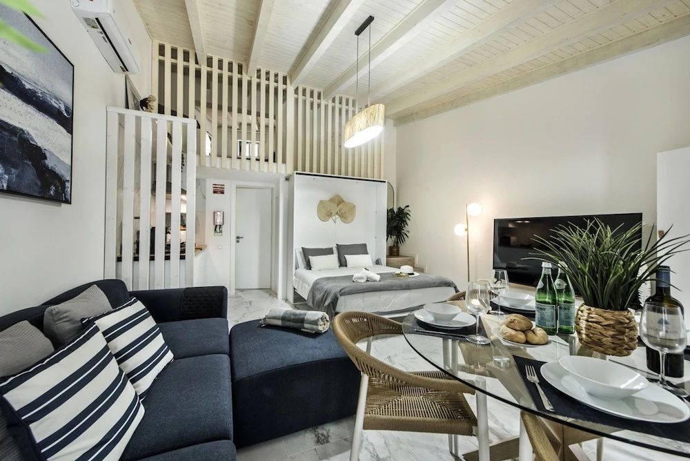 Modern eingerichteter Wohnbereich mit dunklem Sofa, Esstisch und Fernseher.