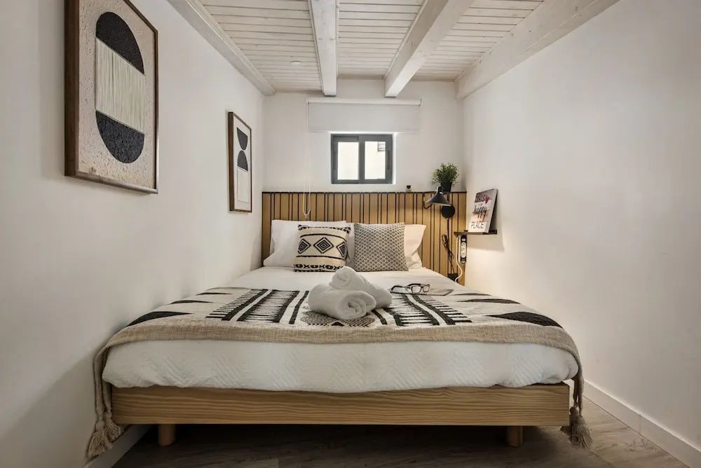 Doppelbett mit gemusterter Tagesdecke und Handtüchern unter einer Holzbalkendecke.