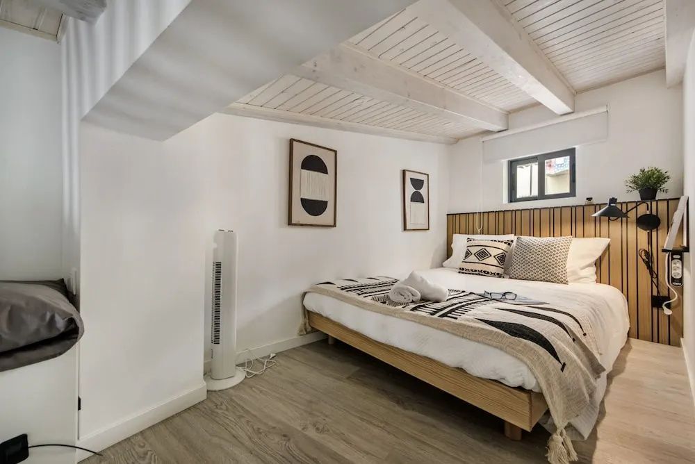 Doppelbett mit gemusterter Decke unter einer hellen Holzkonstruktion mit kleinem Fenster.