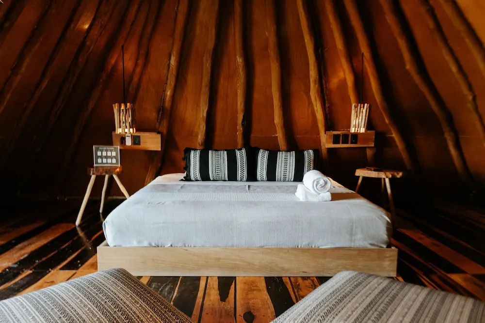 Doppelbett mit hellem Überzug in einem Raum mit rustikaler Decke aus Holzstämmen.