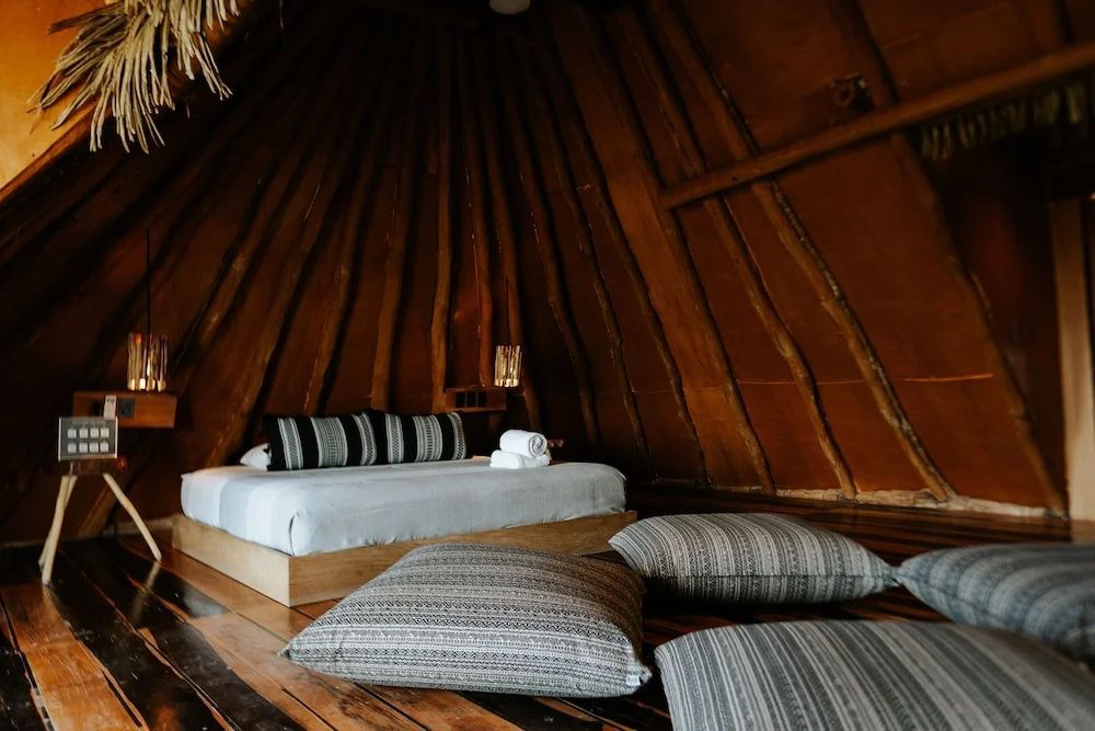 Blick in den Wohn- und Schlafbereich mit Kissen auf dem Holzboden und einem Bett.