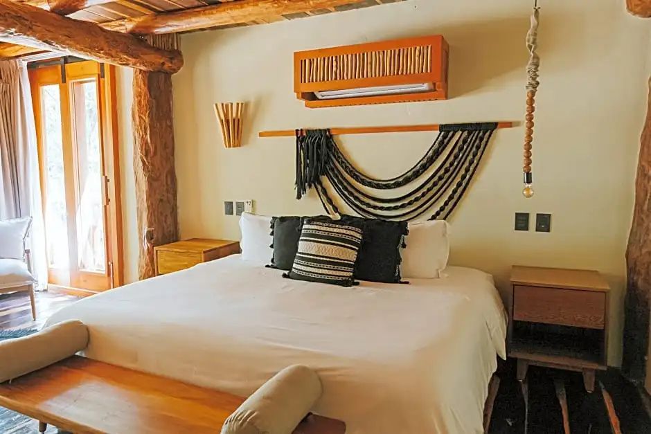 Doppelbett mit Kissen und gewebtem Wandbehang unter einer Holzdecke.