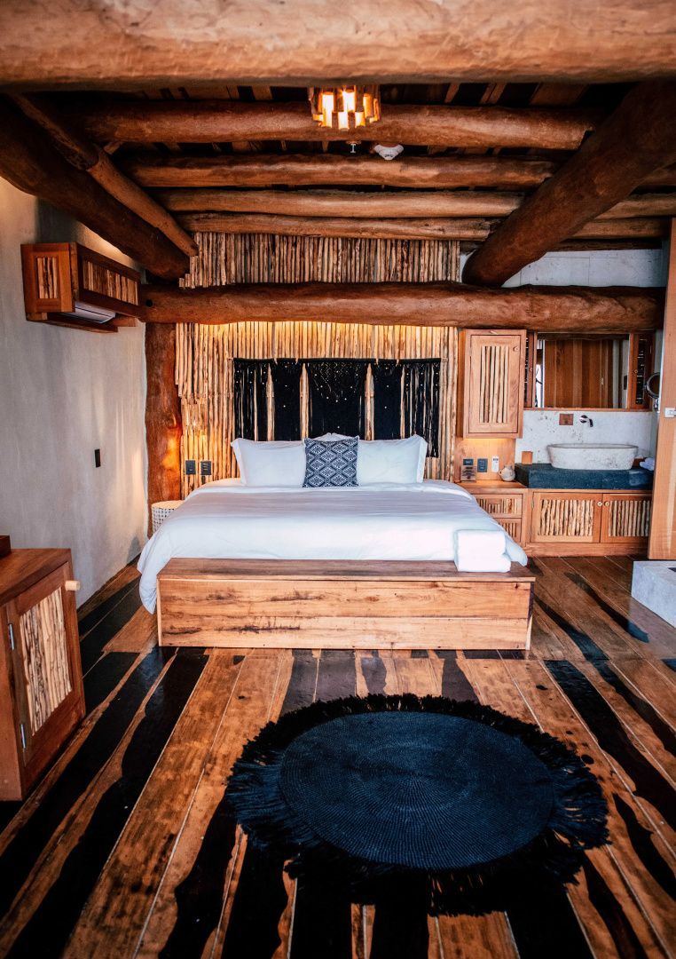 Doppelbett mit weißer Bettwäsche, rustikaler Holzdecke und rundem schwarzem Teppich.