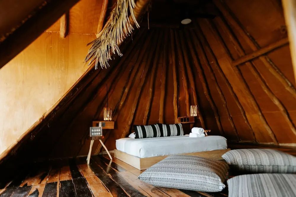 Geräumiges Zimmer mit spitz zulaufender Decke aus Holzstämmen und Holzboden.