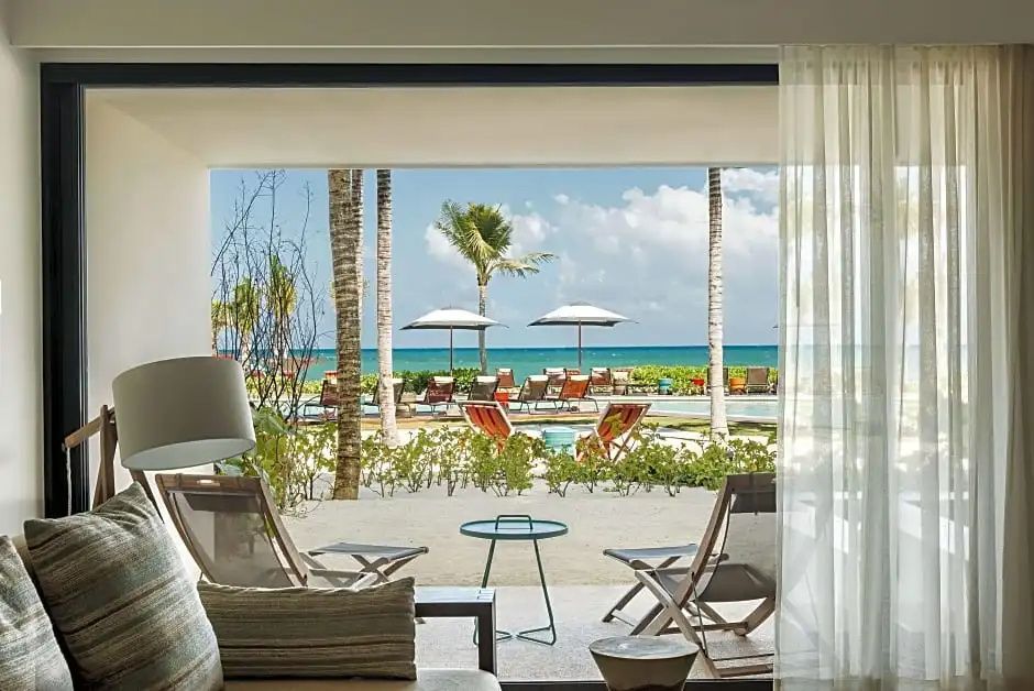 Blick von der Terrasse auf den Sandbereich, Liegestühle, Palmen und das Meer.