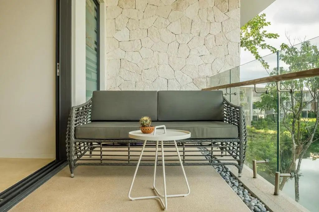 Graues Sofa und ein beistellender runder Tisch auf dem Balkon vor einer Steinwand.